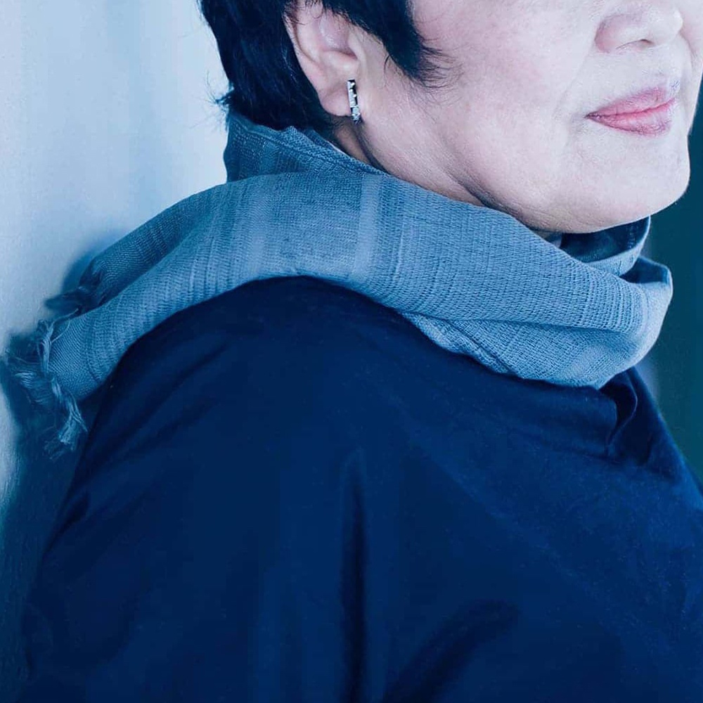 一位女性佩戴著一條淺灰色今治匹馬棉圍巾，圍巾帶有細緻的格紋圖案和流蘇邊緣。