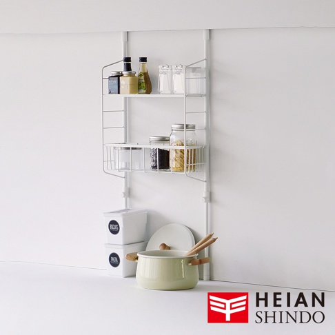 白色金屬網架收納架，附有兩層置物籃，上方籃架擺放著玻璃罐裝調味料及瓶裝醬料，下方籃架則有玻璃罐裝的餅乾、黑豆和義大利麵。收納架下方有兩個白色儲物盒，其中一個標示「BISCUITS」，另一個標示「PASTA」。旁邊擺放著一個淺綠色附蓋湯鍋，鍋柄為木質，鍋內插有兩支木筷。