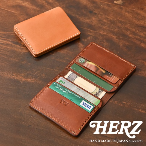 日本HERZ 職人手作皮革鈔票夾，內有信用卡、日圓鈔票，下方印有HERZ LOGO，後方另有一個褐色皮革摺疊皮夾