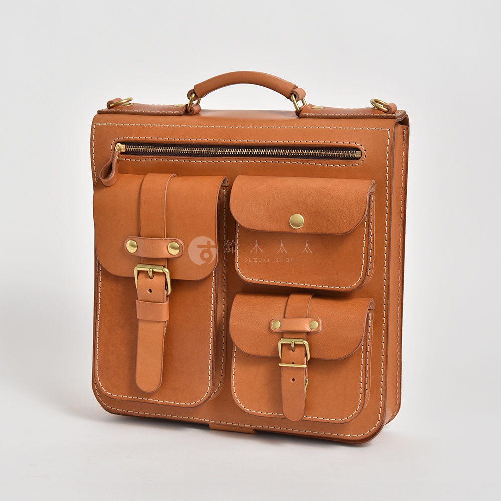職人手作皮革三口袋三用後背包，呈現經典棕色，採用柔軟的皮革材質，配有雙層前袋、帶扣皮帶、黃銅金屬扣件，以及頂部提把和拉鍊開口。