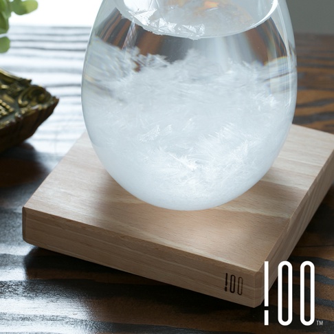透明玻璃製成的 Tempo Drop 天氣瓶，內部充滿細緻的白色結晶，底部放置於淺木色木製底座上，呈現簡約自然的風格。