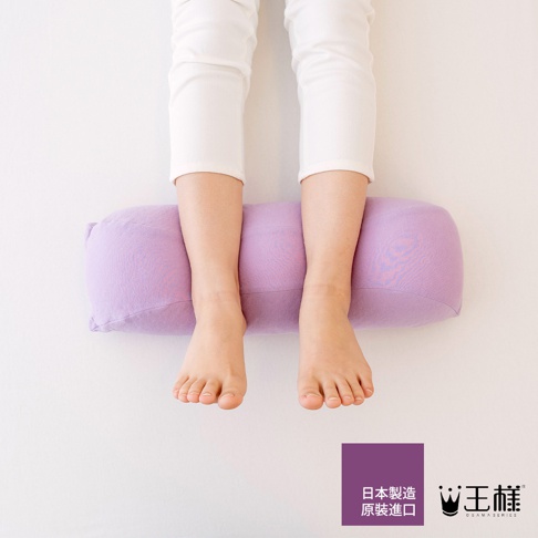 一雙女性裸足踩在一個淡紫色圓柱形抬腿枕上，枕頭材質為柔軟織布。