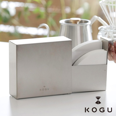 KOGU 珈琲考具日製分隔式不鏽鋼咖啡濾紙收納盒，擺放於檯面上，旁邊是咖啡壺與咖啡濾杯。
