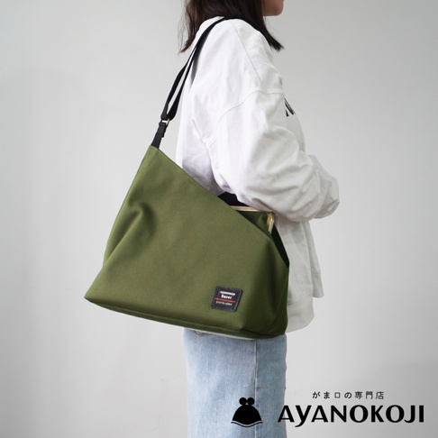 一位身穿白色連帽衫和淺藍色牛仔褲的女士，肩上斜挎著一個軍綠色的方形口金單肩包，包上有 AYANOKOJI 的標誌