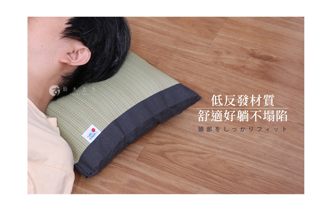 藺草編織的枕頭，淺綠色枕面配深藍色條紋滾邊，枕頭一角貼有「made in Japan」標籤，枕頭置於木質地板上，部分畫面顯示人側臥的頭部。