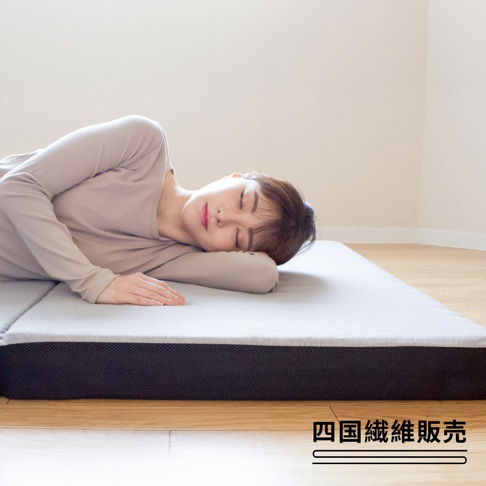 一位女性側臥在灰色三折床墊上。床墊有著網狀織物的側面，放在木質地板上。