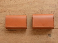 兩個淺棕色牛皮證件夾，以縫線裝飾邊緣，放置在木紋背景上。