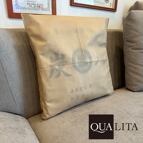 QUALITA 炭八專用防塵套，以淺褐色環保材質製成，表面印有炭的圖案與日文說明，放在灰色沙發上。