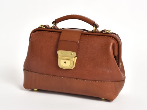 棕色皮革製成的迷你口金包，配有手提把、可拆卸肩帶金屬扣環，以及黃銅色鎖頭和底部腳釘，整體呈現復古醫藥包造型。