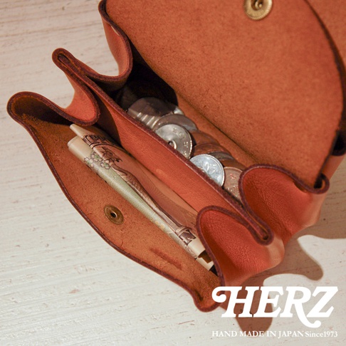 焦糖色皮革三層零錢包，內有日圓紙鈔與硬幣，風格簡約。