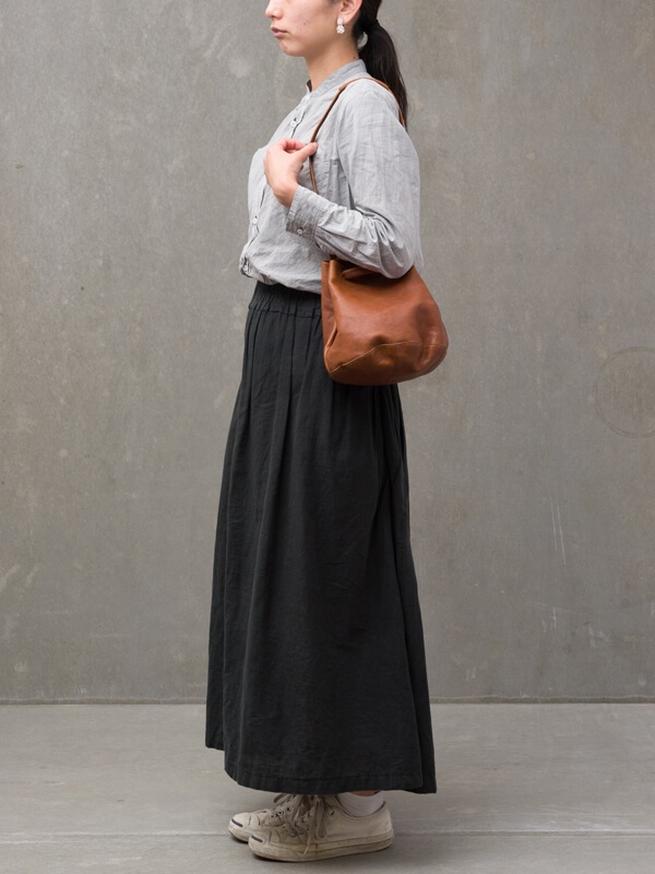 一位女士身穿灰色襯衫和黑色長裙，斜肩背著一個棕色皮革抽繩水桶包。
