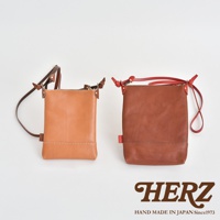 職人手作皮革直式隨身單肩包，左側為淺褐色皮革，右側為深褐色皮革，兩款包皆為直向方形設計，配有可調節式皮革背帶及拉鍊開口，展現簡約質感。