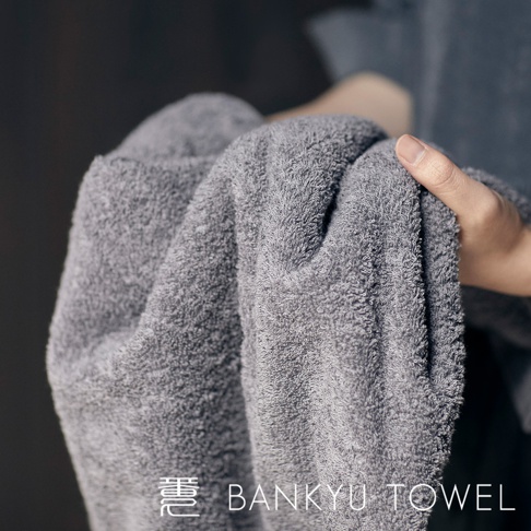 灰色長纖浴巾，質地柔軟，帶有立體紋理，由細長纖維製成，觸感蓬鬆，適合日常使用。