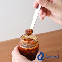 銀色不鏽鋼萬用醬料小勺，勺頭沾滿紅褐色香辣醬，一隻手拿著裝有醬料的透明玻璃瓶，另一隻手則握著小勺。