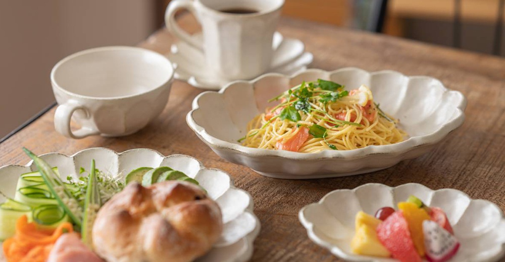 白色美濃燒六魯粉引湯杯碗，搭配花形淺盤，盛有義大利麵、沙拉及水果，置於木紋桌面上。