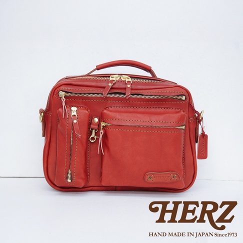 紅色皮革兩用收納單肩包，採用職人手作工藝，設有多個拉鍊口袋和隔層，搭配金色拉鍊和吊牌，展現質感。