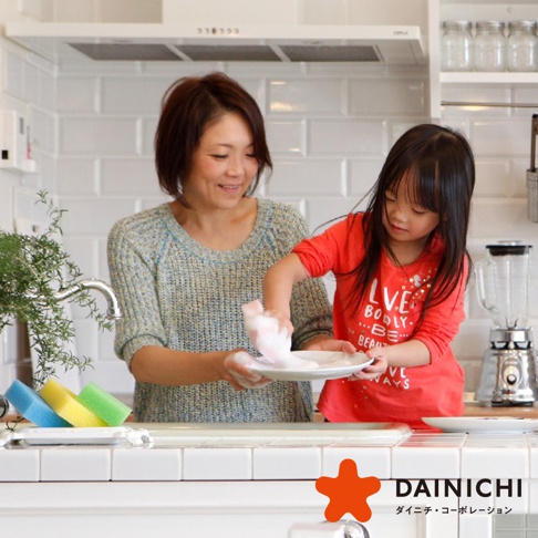 廚房水槽旁，一位母親和女兒正一起洗碗，桌上擺放著藍色、黃色和綠色的四個海綿。