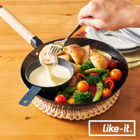 黑色鐵製調理鍋，配有木製手柄，鍋內盛有起司醬，旁邊是烤蔬菜和麵包塊，由叉子夾取一片沾有起司的麵包。