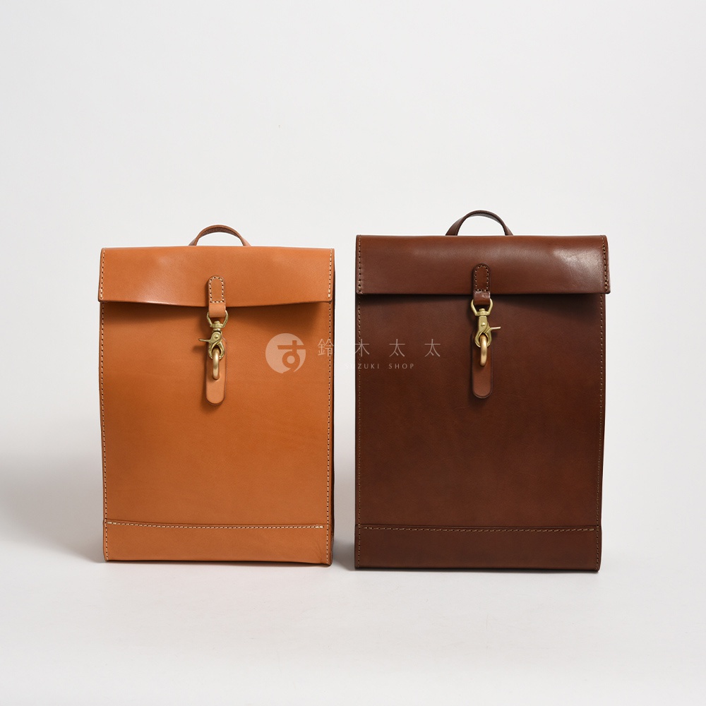 兩個紙袋風後背包，右邊為深棕色，左邊為淺棕色，皆為皮革材質，設有金屬鉤扣開合，展現職人手作質感。