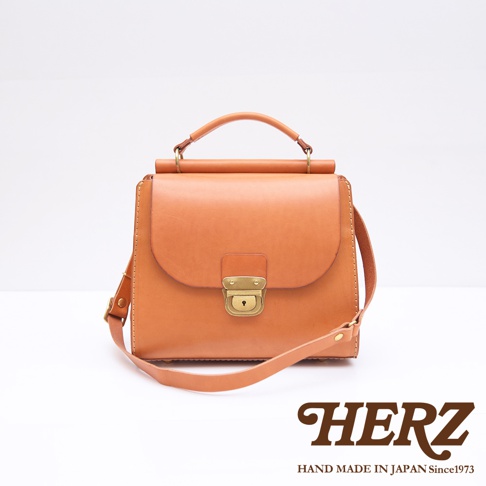 HERZ 品牌標誌旁的日製手工皮革兩用包，為咖啡色瓦風設計，搭配金色鎖頭與提把。