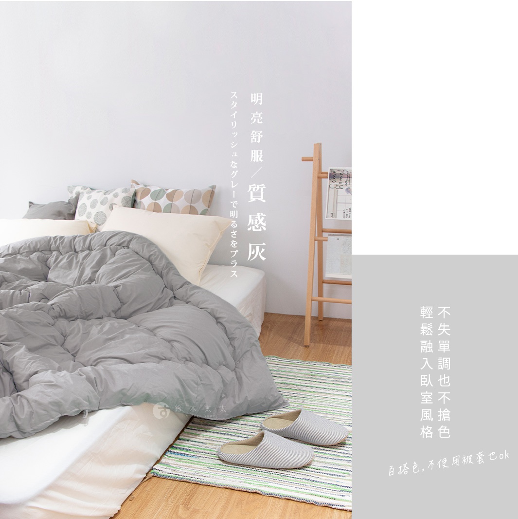 床鋪上鋪著一條灰色的蓬鬆棉被，旁邊有幾何圖案的抱枕，左側是木製的雜誌架，右側印有日文和中文的廣告語，地上有兩雙室內拖鞋。