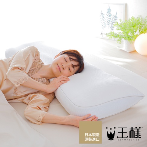 一位女子側臥於白色床鋪上，臉頰倚靠在白色網格紋理的「王樣のWide&Long 極夢枕」上，枕頭材質看起來柔軟且有支撐感，整體畫面呈現寧靜舒適的睡眠氛圍。