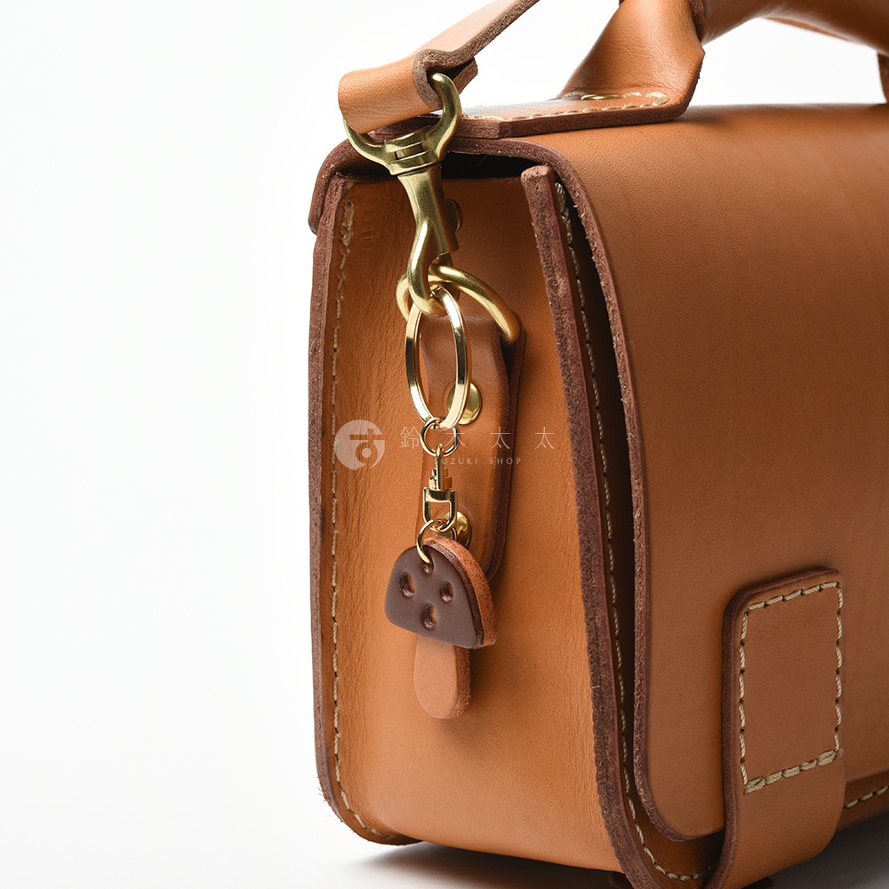 職人手作皮革香菇造型鑰匙圈，附有黃銅掛環及鉤扣，吊飾為咖啡色皮革製香菇造型，傘蓋處有三個圓形孔洞。