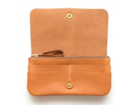 淺棕色皮革長夾，有掀蓋式設計，內含多層卡槽、拉鍊零錢袋，以及一個小皮質拉環，整體風格簡約。