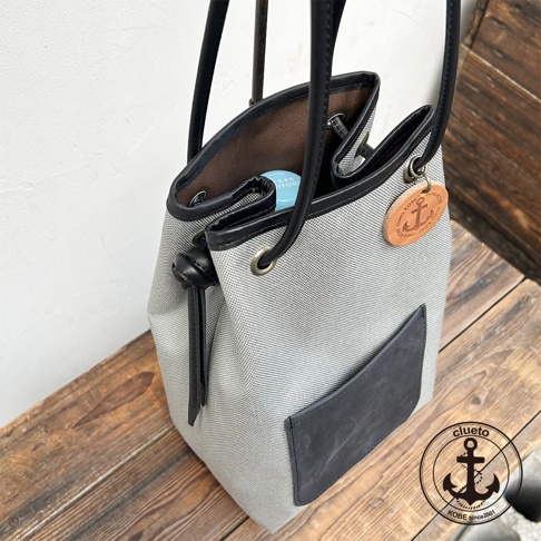 神戶clueto品牌，nico防潑水尼龍與義大利皮革製成的灰色束口水桶包，配有品牌皮革吊飾與前方皮革口袋