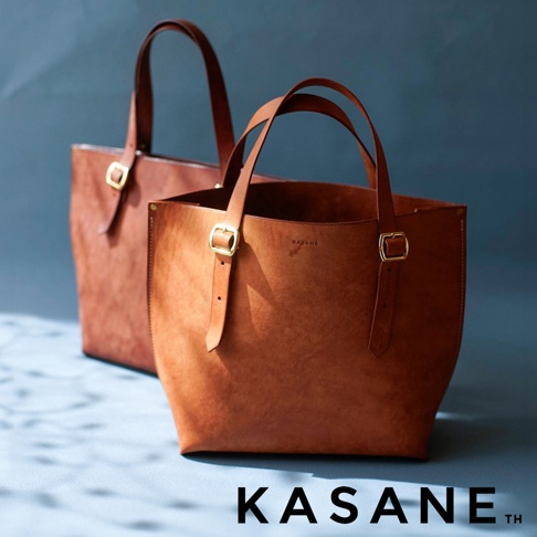 這是一個帶有金色搭扣的皮革托特包，包包上印有 KASANE 字樣。