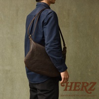 職人手作深棕色皮革單肩半月包，斜挎於穿著深藍色襯衫的男性身上，包身呈現自然的皮革紋理。