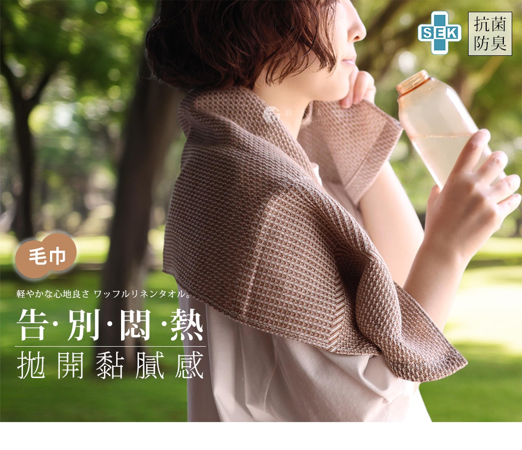 一位女士肩上披著一條棕色格子毛巾，手裡拿著一瓶水，背景是綠色的樹林。