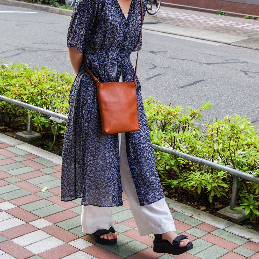 一名女子身穿印花長洋裝，肩背一個棕色皮革製的方形小包。