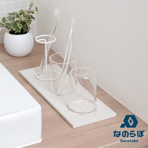 白色條紋珪藻土置物墊，上面擺放著兩個透明牙刷杯，其中一個杯子內有牙刷，另一個杯子倒蓋著，以及一個白色金屬牙刷架。