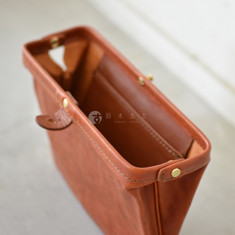 職人手作皮革Organ手拿包，呈現溫潤的棕褐色，細緻車縫線與金屬釦點綴，展現皮革的自然紋理與質感。