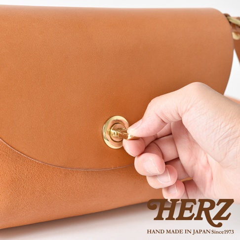 職人手作皮革迷你單肩手袋 CK-11，展示棕色皮革的質感和金屬鎖扣的細節，手部正在操作鎖扣。