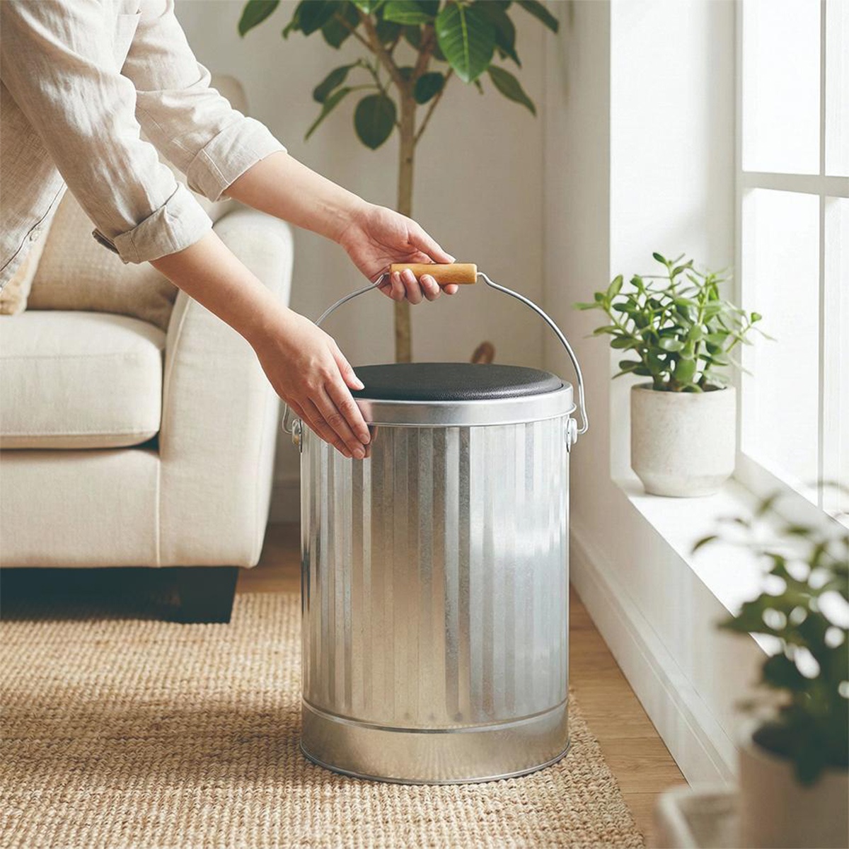 一個帶有木質把手的銀色鍍鋅鋼儲物桶，上面有一個黑色坐墊，可以當作椅子使用。