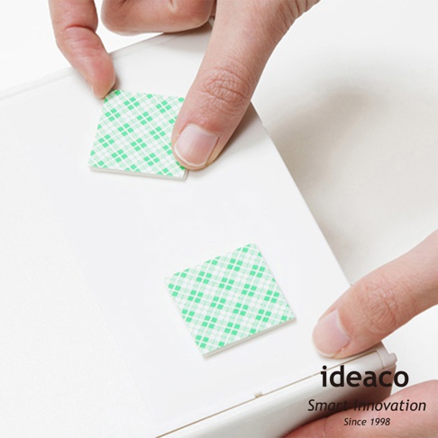 兩塊綠色格紋雙面膠帶被手指按壓在白色平面上，右下角印有「ideaco Smart Innovation Since 1998」字樣。