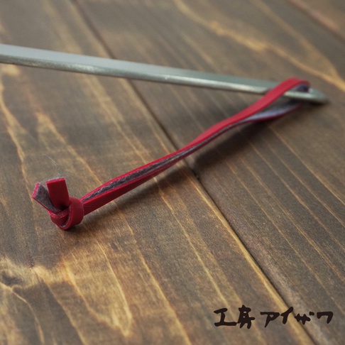 不鏽鋼萬用瀝水湯勺的細節特寫，展示了湯勺金屬本體與紅色皮革掛繩的連接處，掛繩由兩層皮革製成，內層為灰色，外層為紅色，並以一個小繩結固定。