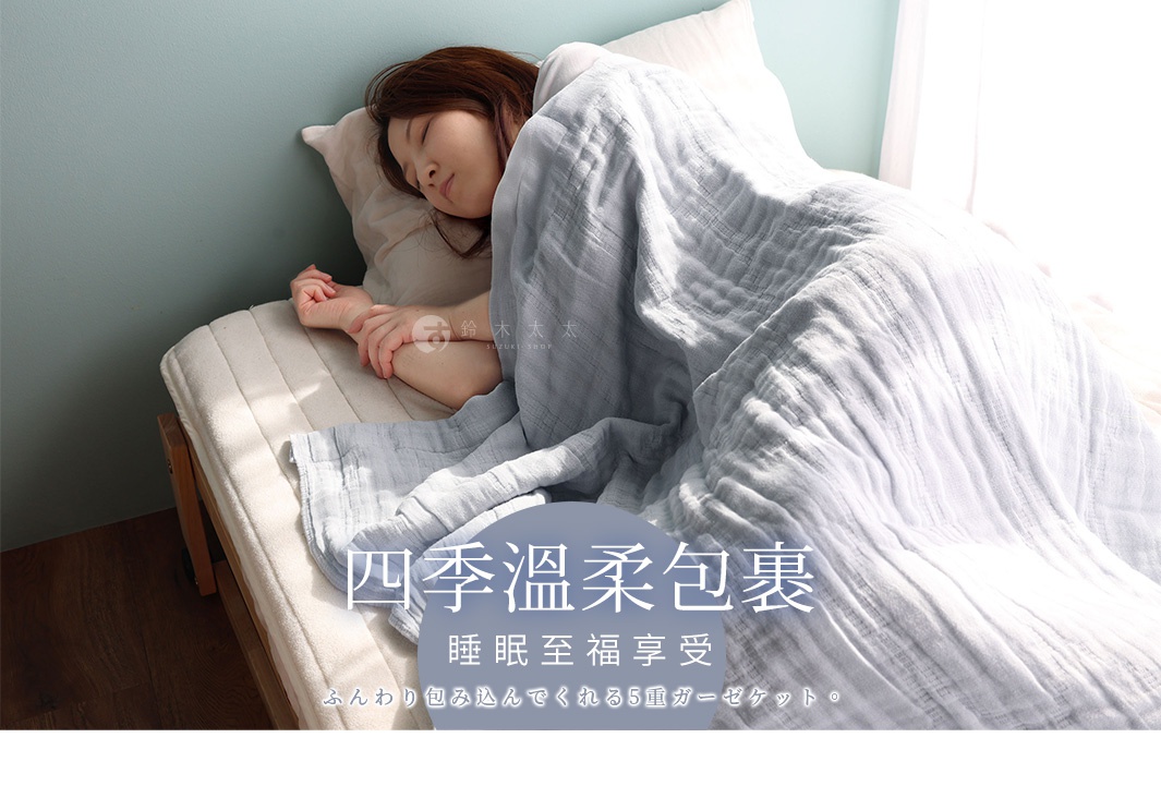 一位女性在舒適的床上蓋著淺藍色多層紗布被子，被子上印有日文，表示「四季溫柔包覆，睡眠至福享受，蓬鬆包覆的五層紗被」。