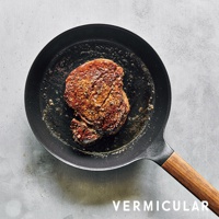 日本製Vermicular鑄鐵平底深鍋，黑色鍋身搭配木質手柄，鍋中煎著一片金黃香煎牛排。