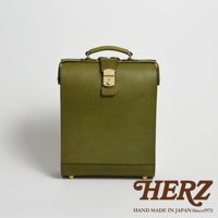 橄欖綠皮革製成的職人手作杜勒斯商務後背包，正面有一個金色旋鈕鎖扣及提把，底部有四個金屬腳釘，風格簡潔復古。