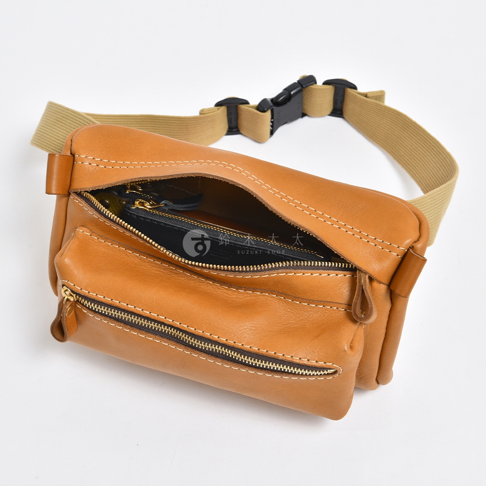 棕色皮革製成的手拿包，帶有卡其色織帶和黑色搭扣。包包有兩個拉鍊口袋，其中一個已打開，露出內部。