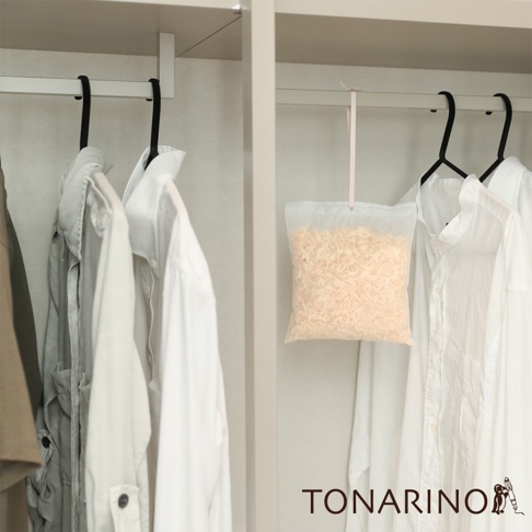 一個透明的防潮消臭檜木除濕包，內含淺棕色的檜木碎屑，懸掛在衣櫃的掛桿上，旁邊有幾件白色衣物。
