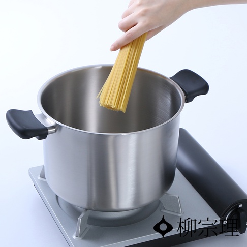 一只手正在將一束義大利麵放入一個霧面不鏽鋼雙耳高鍋中。高鍋為銀色，配有黑色手柄。