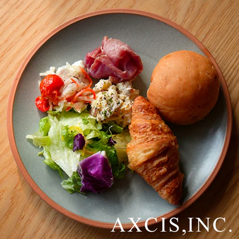 PURE 素燒百搭陶瓷主菜盤 M，盤面為灰綠色，邊緣帶有陶土原色，盤中盛有沙拉、麵包、可頌與火腿。