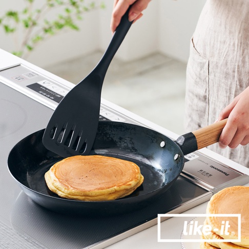 黑色萬能調理鐵鍋，鍋內煎著金黃色鬆餅，旁有黑色排油槽鍋鏟，鍋柄為木質。