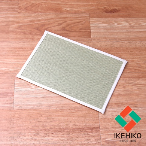 淺綠色藺草編織枕墊，邊緣有白色包邊，放置於淺棕色木紋地板上。