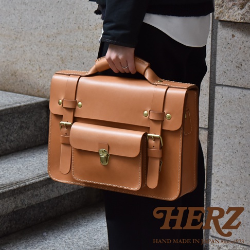 職人手作皮革學院風兩用商務公事包 BC-16，淺棕色。包包為方形設計，採用厚實的皮革材質，配有金屬釦環、插銷和皮帶設計。雙層前袋，提把和側邊皆有車縫線裝飾。