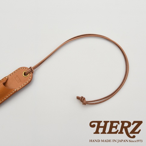 簡約的棕色皮革筆套，配有細長的皮繩，繩子上打著兩個結，下方印有HERZ品牌標誌和HAND MADE IN JAPAN Since1973字樣。